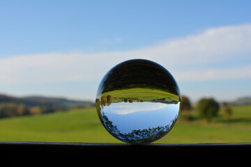 Green landscape reflected in a sphere, with blue sky
