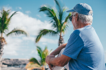 Rear view of relaxed senior bearded man sitting outdoors face the sea enjoying sunny day, travel, vacation, retirement