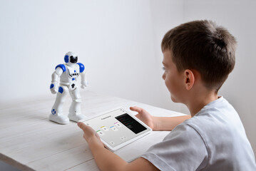 Boy is programming the work of a robot on a desk with a tablet in his hand