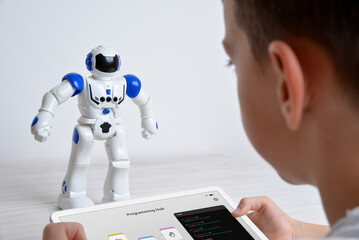 Boy controls robot using tablet on desk. Illustrating education, technology, innovation, and...