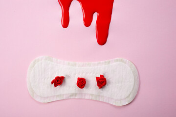 Blood and feminine hygiene pad with red flowers on pink background. First menstrual period concept 