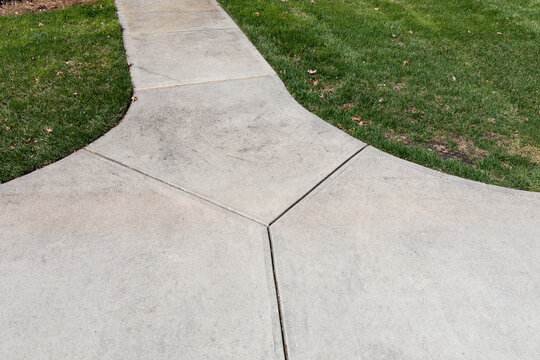 Broad concrete area leading off into a narrow path bordered by grass, creative copy space, horizontal aspect