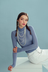 Fashionable confident woman wearing blue turtleneck, layered pearl necklace, white denim skirt, posing on blue background. Copy, empty, blank space for text