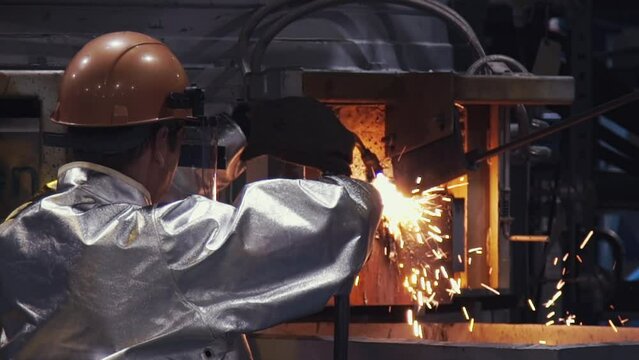 Male Worker In Protective Uniform Using Welding Torch At A Metallurgy Factory. Industrial Welding Torch Worker In Steel Making Production Process. Welding Torch Worker Manually Fusing Metal Parts