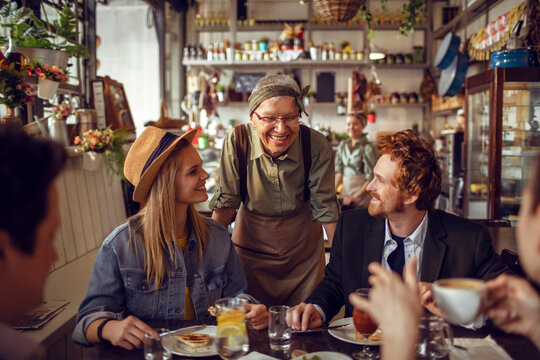 Senior waitress small restaurant owner serving a young group of people
