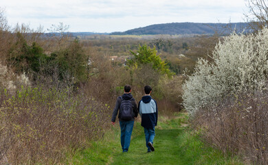 Fototapeta na wymiar Father and his adolescent son (unrecognizable; back view) walking on a hiking path near Moret-sur-Loing. Springtime in Ile-de-France, France. Spring holidays nature travel background.