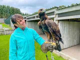 PORTRAIT: Smiling visitor at falconry center holding a golden eagle on her hand