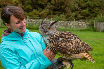 PORTRAIT: Cheerful lady with a beautiful Eurasian eagle owl perched on her arm