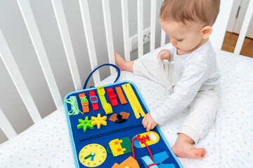 Baby playing with busy book sitting in crib. Concept of smart books and modern toys