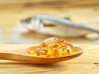 A vibrant wooden spoon filled with fish oil capsules, set against the backdrop of a fish, visually highlighting the source and benefits of the supplement.