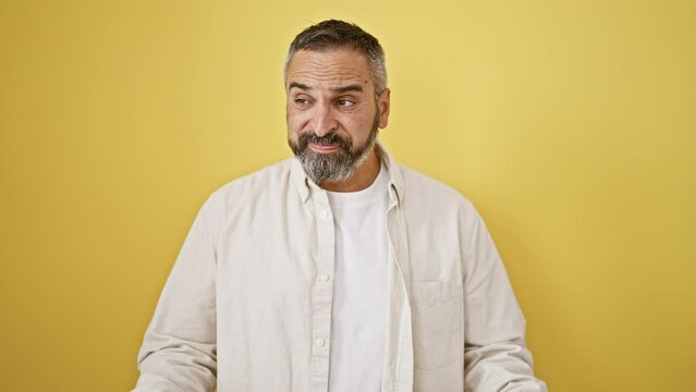 Mature bearded man in white shirt expressing discomfort against yellow background