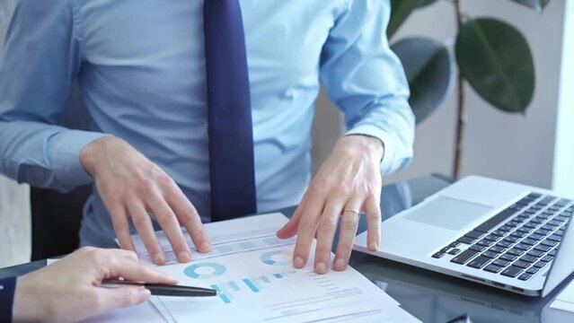 Businessman and woman analyzing data at glass desk beside a laptop in modern fair office, close up view. Business concept