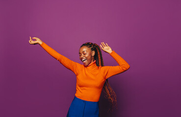 Happy african woman celebrating in colourful casual clothing against vibrant purple background