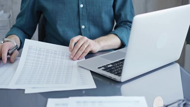 Businessman or professional auditor is analyzing data on laptop. Person in a blue shirt works with data sheet. Business concept