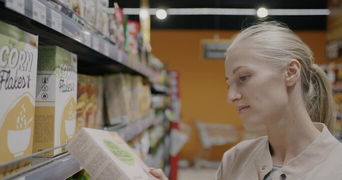 Young lady choosing healthy product taking box from shelf in supermarket shopping in grocery store. Nutrition and organic food concept.