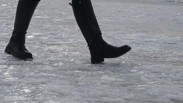 A person in black boots is standing on the snowy ground, their foot leaving imprints in the icy flooring as they gesture with their hands to balance themselves