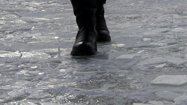 A persons human leg in black boots walking on icy flooring over a frozen lake, with knee and thigh exposed to cold wind waves