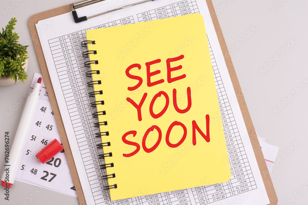 Poster see you soon text written on notebook page. office desk table top view