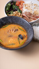 Tom yam soup with seafood and bowl with rice, veal and vegetables angle view