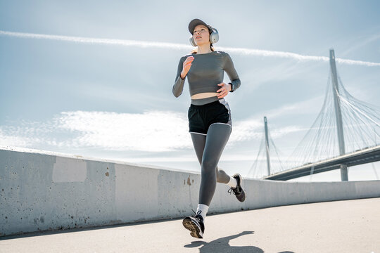 Dedicated female runner jogging on a bridge with headphones and clear blue skies.
