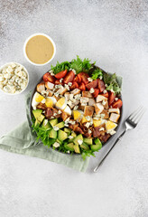 American Cobb salad with tomatoes, bacon, chicken, eggs, avocado, blue cheese on gray background. Top view. 