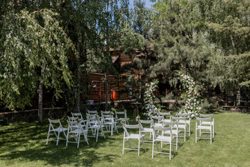 Outdoor wedding ceremony with a stunning floral arch and white chairs set in a serene garden