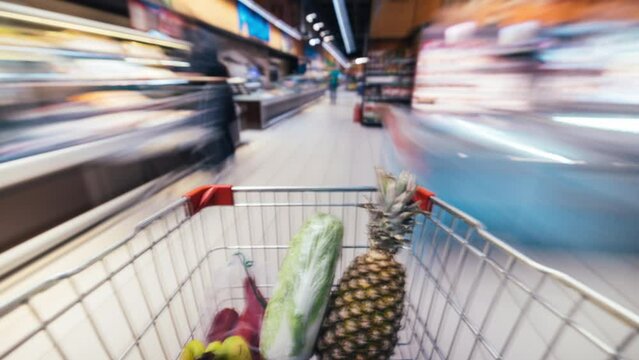Time lapse of shopping cart moving between aisles and sections of supermarket full of healthy food products. Groceries and consumerism concept.