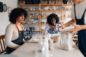 Interracial pottery class attendees sitting at pottery studio with tutor.