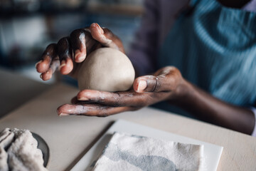 Close up of interracial craftswoman's hands modeling clay at workshop.