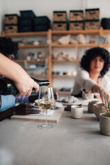 Hand pouring wine on pottery class with students in background.