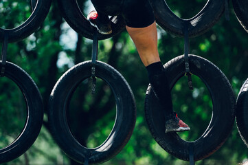 Woman legs while climbing over the wall made or car tires during an OCR race