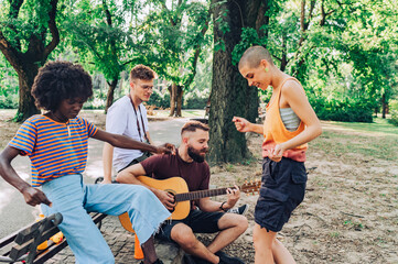 A group of interracial friends having fun with guitar at the park.
