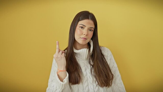 Rude show-off! young, beautiful hispanic woman in sweater, giving you the 'fuck you' sign, a crazy impolite gesture with a middle finger, standing over an isolated yellow background.