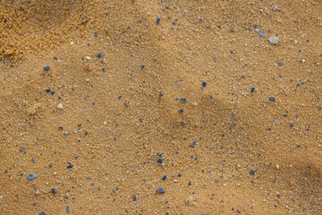 Close up of sand with scattered small blue and grey pebbles. The texture of the sand is finely granulated and the pebbles are irregularly shaped. Golden sand, the colorful pebbles and natural pattern