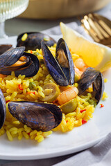 Paella with mussels and shrimps, on white plate, served with lemon and white wine, vertical closeup