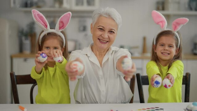 Easter grandmothers with granddaughters. Smiling grandmother with twins grandchildren painting decorating colorful eggs in rabbit bunny ears, celebrate at home. Easter happy holiday concept.