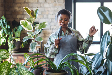 Beautiful cheerful joyful plus size African American young woman repotting home green plants,...
