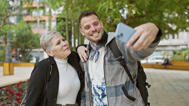 A woman and a man happily taking a selfie together outdoors in an urban park, showcasing a friendly or familial bond.