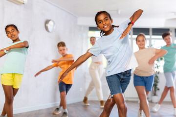 Smiling african american preteen boy dancer practicing active vigorous dance with group in modern studio..