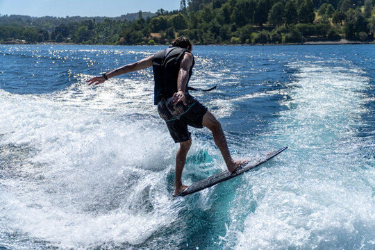 Athletic young man wake surfing on a wave in the lake, spinning mid-air doing a trick.
