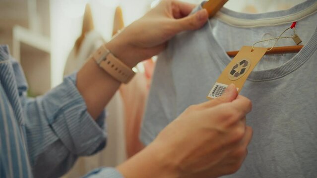 Recycling signs. Modern woman dressed in fashionable outfits inspects racks of clothes in stylish store where recycling signs are highlighted. She holds a tag with a recycling symbol, showing interest