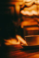 A cup of coffee standing on a wooden table illuminated by warm yellow light in a cozy jazz cafe. - 762758002