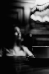 A cup of coffee standing on a wooden table illuminated by warm yellow light in a cozy jazz cafe and a mysterious girl on a background. Black and white. - 762758014