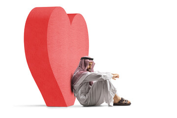 Sad saudi arab man sitting on the ground next to a big red heart