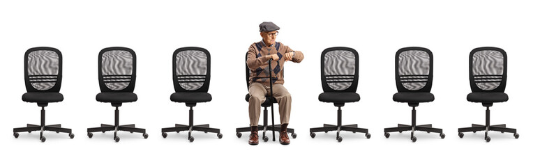 Empty office chairs and an elderly man sitting and checking his watch