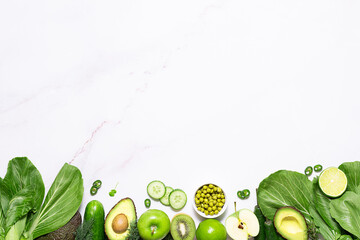 Food frame made with fresh green vegetables, herbs and fruit on white marble background with copy space for your design top view. Healthy vegan food concept.
