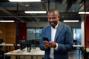Happy mature black man in businesswear using mobile phone in office - 762777831