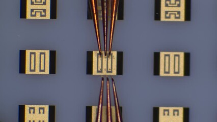 Radio requency probe touchdown and manipulation on calibration substrate at microchip probing station. Microscope view. - Powered by Adobe