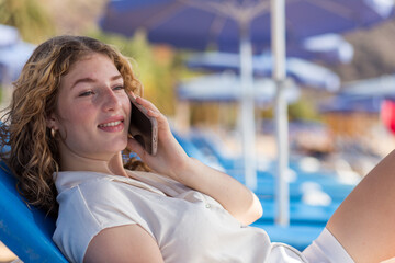 A woman is sitting on a blue beach chair and talking on her cell phone