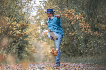 A best ager man kicking a teddy bear in a forest in autumn outdoors
